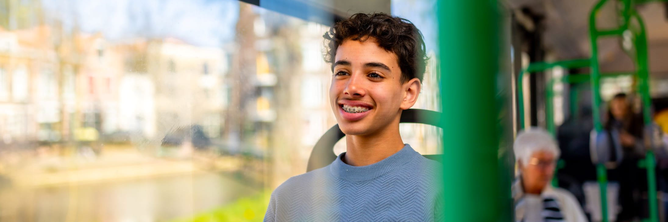 Jonge jongen met donker haar zit glimlachend in de bus aan de kant van het raam